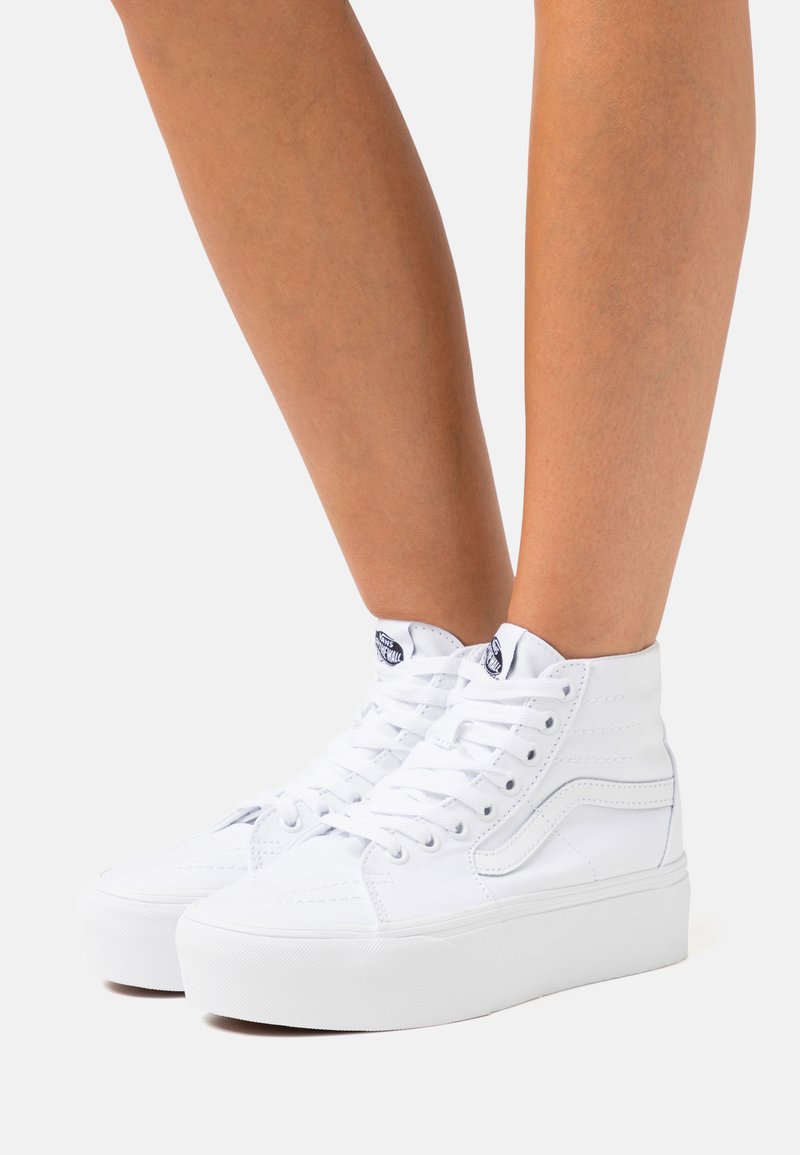 Hvide højtop sneakers med en tekstureret canvas-overdel, snørebåndsdesign og en tyk hvid gummisål. Har stikninger og et logomærke.