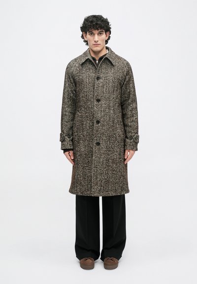 Brauner Tweed-Mantel mit Kragen, Vorderknöpfen und Manschettendetails, kombiniert mit schwarzen Hosen und braunen Schuhen.