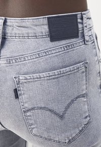 Jean en denim délavé clair avec une surface texturée. Présente une poche visible et un patch en cuir foncé avec un logo embossé à la taille.