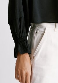 Sort, letvægts bluse med en let cropped pasform og forsumpede ærmer. Kombineret med lyse, tapered jeans med en synlig knap.