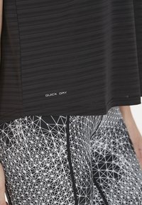 Musta urheilupaita, jossa on käytetty teksturoitua kuviota ja "QUICK DRY" -merkki, yhdistettynä mustiin legginsseihin, joissa on geometrinen valkoinen kuvio.