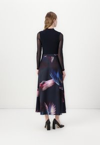 Robe à manches longues avec un haut noir ajusté et une jupe fluide bleu marine ornée d'un imprimé floral coloré. Chaussures à talons bloqués noires.
