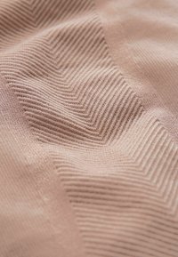Tejido texturizado en un suave tono rosa, con patrones acanalados diagonales y áreas lisas, creando profundidad e interés visual sutil.