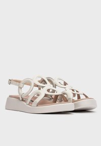 Sandalias blancas con recortes circulares, diseñadas con material sintético y una suela de cuña baja. Correa trasera con hebilla ajustable para un mejor ajuste.