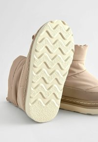 Tan geïsoleerde laarzen met een gestructureerde witte rubberen zool met zigzagpatronen. Zachte, puffy bovenkant met gestikte accenten voor duurzaamheid.