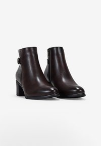 Par de botas de cuero marrón oscuro hasta el tobillo con tacones cuadrados, cremalleras laterales y partes traseras texturizadas con detalle de botón decorativo.