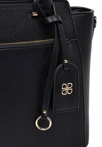 Black textured leather handbag with gold zipper, matching tag with gold emblem, leather strap, and gold ring detail.
