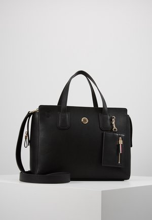 Czarna torebka z teksturowanej skóry z dwoma uchwytami, odpinanym paskiem na ramię, złotym emblematem logo oraz małą przymocowaną saszetką na zamek.