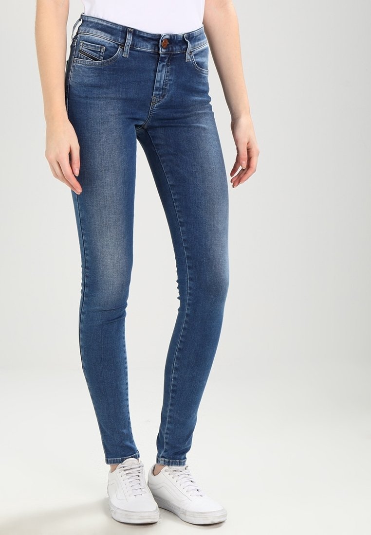 Vaqueros de denim azul ajustados con una cintura de media altura, diseño clásico de cinco bolsillos y un leve efecto desgastado. Combinados con zapatillas blancas.