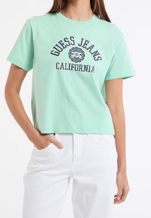 Mint green cotton crop t-shirt featuring a graphic print reading "GUESS JEANS CALIFORNIA" in dark navy, with short sleeves and a relaxed fit.