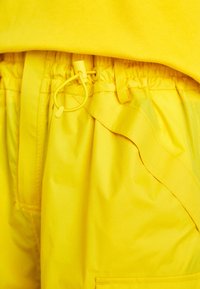 Pantaloni corti gialli realizzati in tessuto leggero con vita elastica e dettaglio con cordino. Texture liscia con una leggera lucentezza.