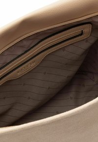 Interior de bolso de cuero beige con bolsillo con cremallera, forrado con tela clara con sutiles rayas diagonales y una etiqueta con el logo en relieve.