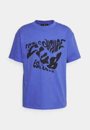 Blå t-shirt med korte ærmer og forvrænget sort tekstgrafik med teksten "THE COUTURE CLUB EST 2015" på fronten.
