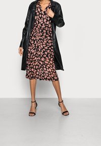 Černý kožený kabát přes růžovo-černé šaty se vzorem a nařasením. Šaty mají krátké rukávy a sahají pod kolena. Černé sandály na vysokém podpatku.