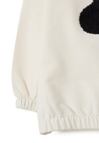 Witte stof met een elastische manchetdetail en een grote textuur zwarte cirkel patch aan de bovenkant aan de rechterkant.