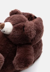 Smešene sobne papuče u obliku smešnog smešnog medveda, smeđe boje, sa mekim, plišanim svojstvima, okruglim ušima i malim belim nosićem sprijeda, dizajnirane za udobnost.