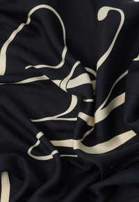 Tela negra con una textura suave que presenta un patrón abstracto y ondulado en color beige. El diseño tiene una apariencia fluida y orgánica con colores en contraste.