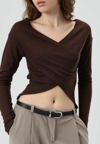 Bruin geribd shirt met lange mouwen, een V-hals en een wikkelontwerp, gecombineerd met beige broek en een zwarte riem met een zilveren gesp.