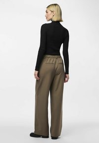 Svart ribbstrikket turtleneck, parret med høytlivde, vide brune bukser med rynket midje og baklommer.