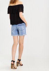 Top negro off-the-shoulder con encaje floral en los bordes, combinado con pantalones cortos de mezclilla azul claro y sandalias de tacón negro.
