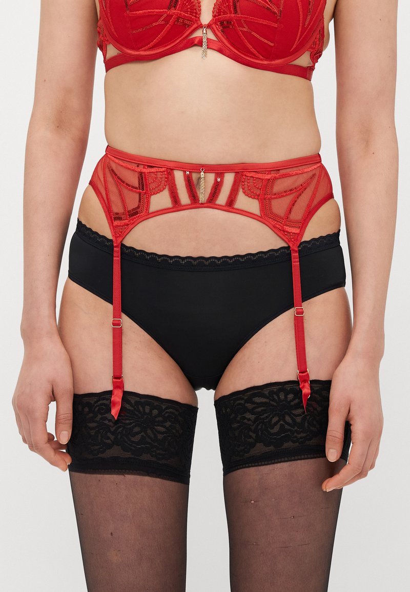 Raudonos nėriniuotos liemenėlės su geometriniu dizainu derinys su juodais, aukštu liemeniu kelnaitėmis. Yra dirželiai kojinėms ir juodos nėriniuotos kojinės su viršutiniais kraštais.