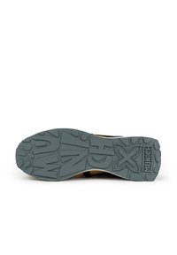 Suela de zapatilla con una superficie de goma texturizada y gris. Presenta surcos profundos y una marca en relieve. En general, un diseño funcional para el agarre.