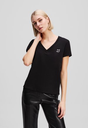 Black cotton t-shirt with a V-neck, short sleeves, and a small white logo printed on the left side. Paired with black leather pants.