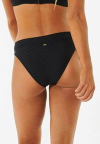 Schwarze Bikinistell mit geripptem Material und hohem Schnitt, ausgestattet mit einem breiten Taillenbund und einem kleinen metallischen Akzent-Tag.