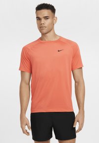 Kortermet treningsskjorte i lys korallfarge med fukttransporterende egenskaper, med en svart Nike-logo på brystet.