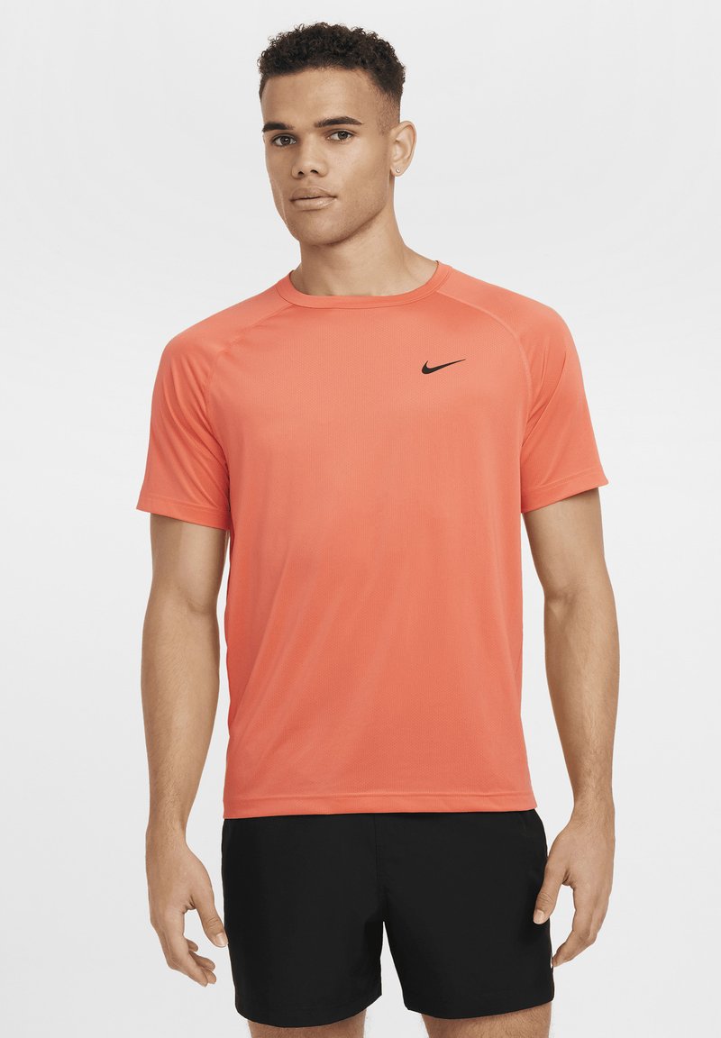 Kortermet treningsskjorte i lys korallfarge med fukttransporterende egenskaper, med en svart Nike-logo på brystet.