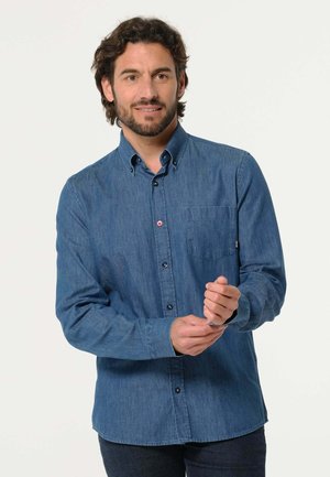Chemise en denim bleu foncé à manches longues avec col boutonné, poche poitrine simple et fermeture à bouton sur le devant. Présente une texture subtile.