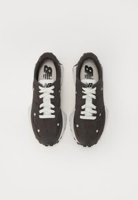 Dunkelbraune Sneakers mit weißen Akzenten, strukturiertem Stoff, floralen Details und auffälligen Schnürsenkeln auf einer grauen Gummisohle.