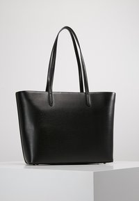 Czarna torba na ramię o gładkiej fakturze, wydłużonym kształcie i dwóch długich uchwytach; cechuje się minimalistycznym designem bez widocznych elementów metalowych czy akcentów.