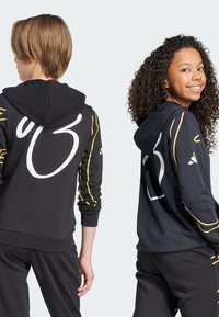 Felpe nere con cappuccio che presentano un grande numero bianco "93" sul retro e dettagli gialli lungo le maniche, realizzate in un materiale morbido.