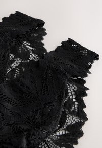 Tissu en dentelle noire avec des motifs floraux et des bords festonnés sur un fond clair.
