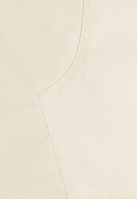 Beiges Gewebe mit einer glatten Textur verfügt über eine gebogene Naht und saubere Nähdetails. Die Oberfläche ist leicht matt.