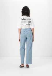 Λευκό μπλουζάκι με μαύρη γραφική εκτύπωση, συνδυασμένο με ανοιχτού γαλάζιες ψηλόμεσες ίσιες παντελόνες. Μαύρες λουράτες γόβες με μυτερές άκρες.