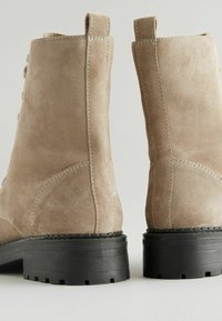 Botines de ante beige con acabado texturizado, punta redondeada y suela de goma negra que presenta un ligero tacón y tiradores laterales.