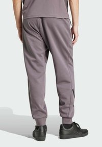 Gray jogger pants with an elastic waistband, tapered ankles, and side pockets. Paired with black sneakers featuring stripe detailing.