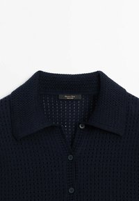 Marineblå strikket cardigan med et tekstureret mønster, der har krave og knaplukninger. Fremstillet af letvægtsstof med et åndbart væv.