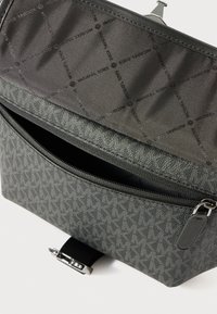 Borsa designer grigia con motivo logo, tasca con zip aperta e rivestimento in tessuto brandizzato, esposta su uno sfondo bianco.