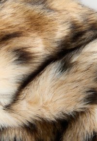 Tissu en fausse fourrure dans des nuances de beige et de brun, présentant des longueurs variées de fibres douces et brillantes avec des rayures plus foncées et de subtiles variations de texture.