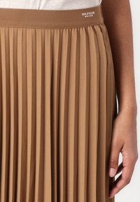 Pleated midi skirt in a light brown color, crafted from smooth fabric. Features a soft waistband with "HILFIGER NEW YORK" logo detail.