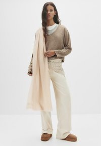 Maglione marrone a maglia sopra una camicia bianca; pantaloni larghi crema con sovrapposizione a motivi; morbida sciarpa rosa drappeggiata; scarpe a piattaforma marroni.