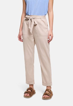 Mujer vistiendo pantalones beige de tiro alto con bolsillos delanteros y cinturón atado, combinados con un top azul sin mangas y sandalias marrones con hebilla.