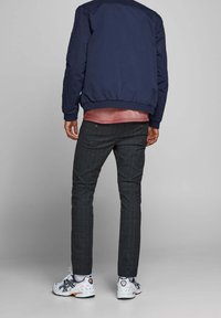 Marinblå bomberjacka över en rosa skjorta. Grå rutiga byxor och vita sportskor med detaljer fulländar outfiten.