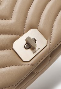 Beige gesteppte Ledertasche mit einem goldenen sechseckigen Verschluss aus Metall. Verfügt über dezente Nähte und eine glatte Oberfläche. Markenname sichtbar.