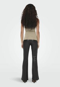 Top de tirantes ajustado beige con una textura suave, combinado con pantalones acampanados negros brillantes de cintura alta, visto desde la espalda.