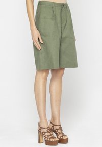Oliwkowe lniane szorty z dopasowanym krojem, z przodu z klapami i zapięciem na zamek. Połączone z brązowymi sandałami na wysokim obcasie.