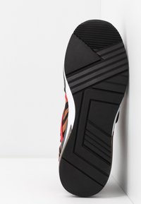 Baskets multicolores avec une tige à motifs, dotées d'une semelle extérieure en caoutchouc noir à rainures texturées pour une meilleure adhérence. Conçues pour un usage sportif.